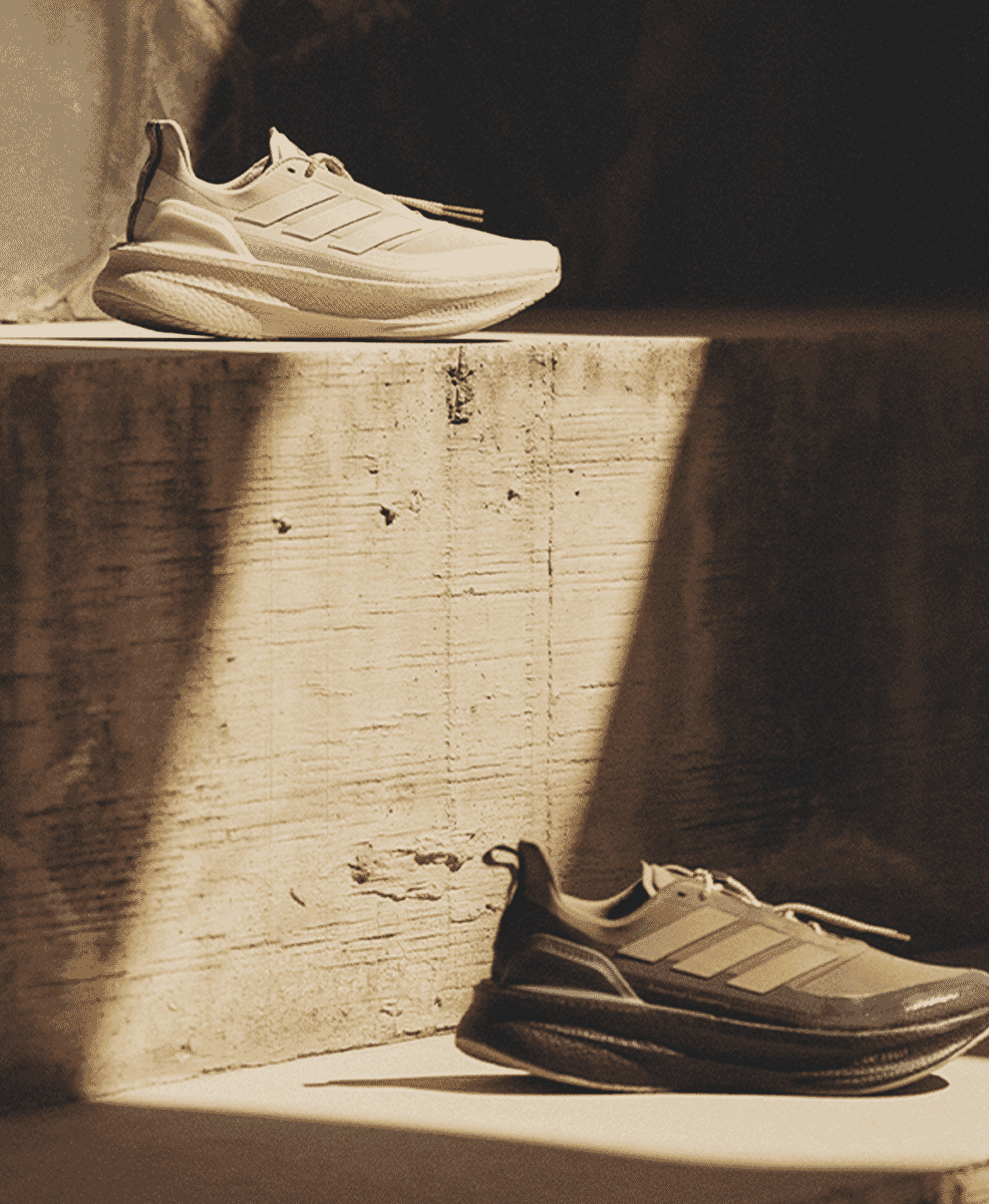 White and dark gray Adidas UltraBOOST 5 sneakers on a concrete ledge with a sepia urban background.