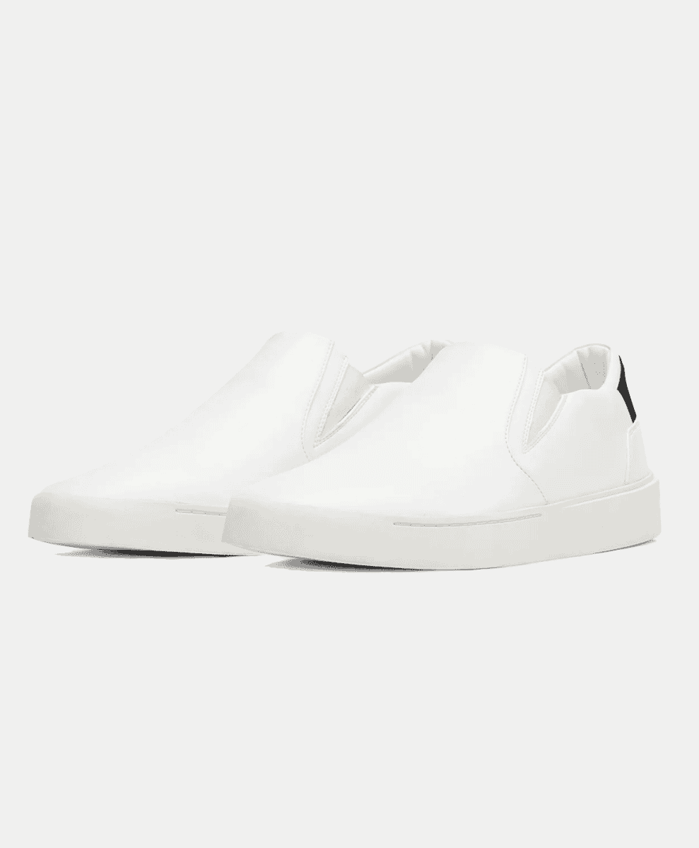 Minimalist white slip-on sneakers with a chunky sole and black heel accent.