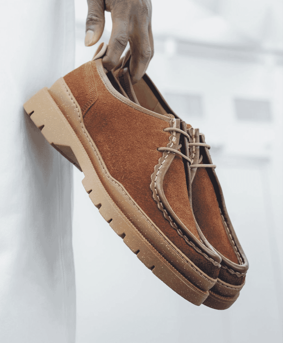 A hand holding a pair of brown suede shoes with chunky beige soles.