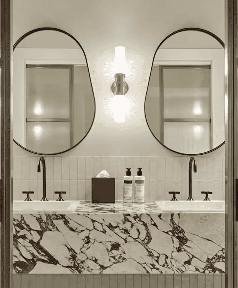 Modern hotel bathroom with marble countertops and oval mirrors.