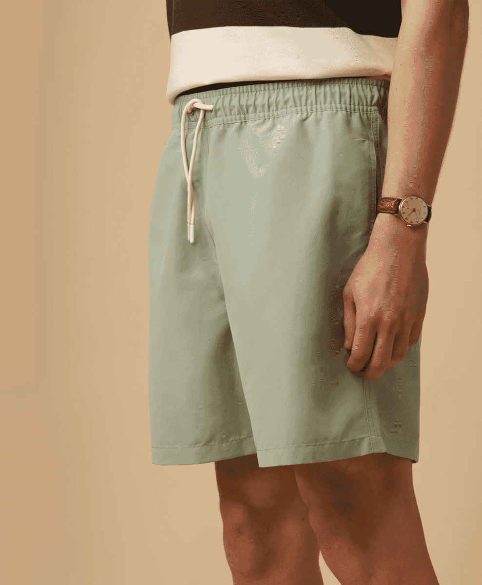 Close-up of light green elastic-waist swim shorts with a watch and t-shirt.