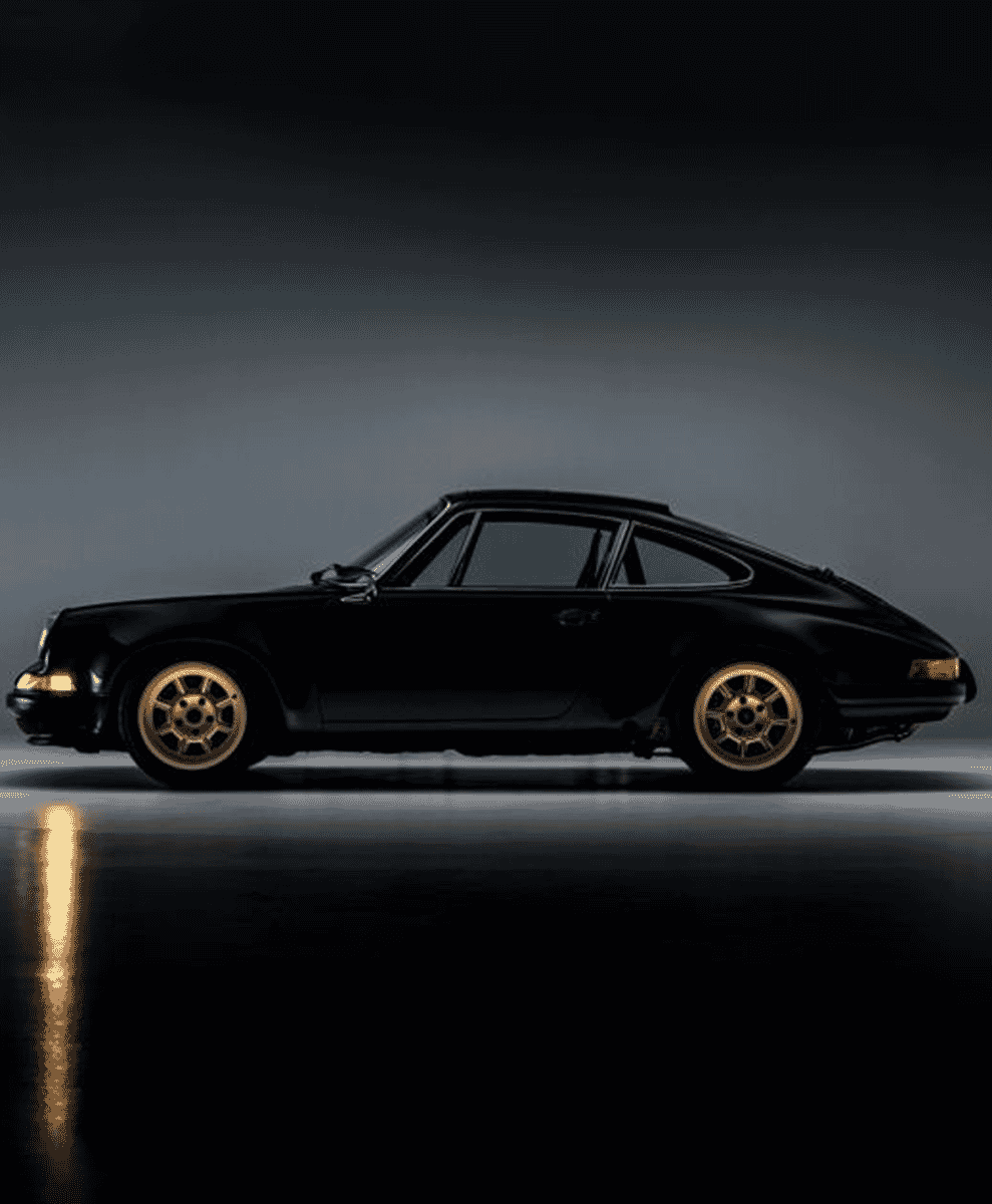 Vintage black sports car with gold wheels in a dramatic studio setting with reflective floor.