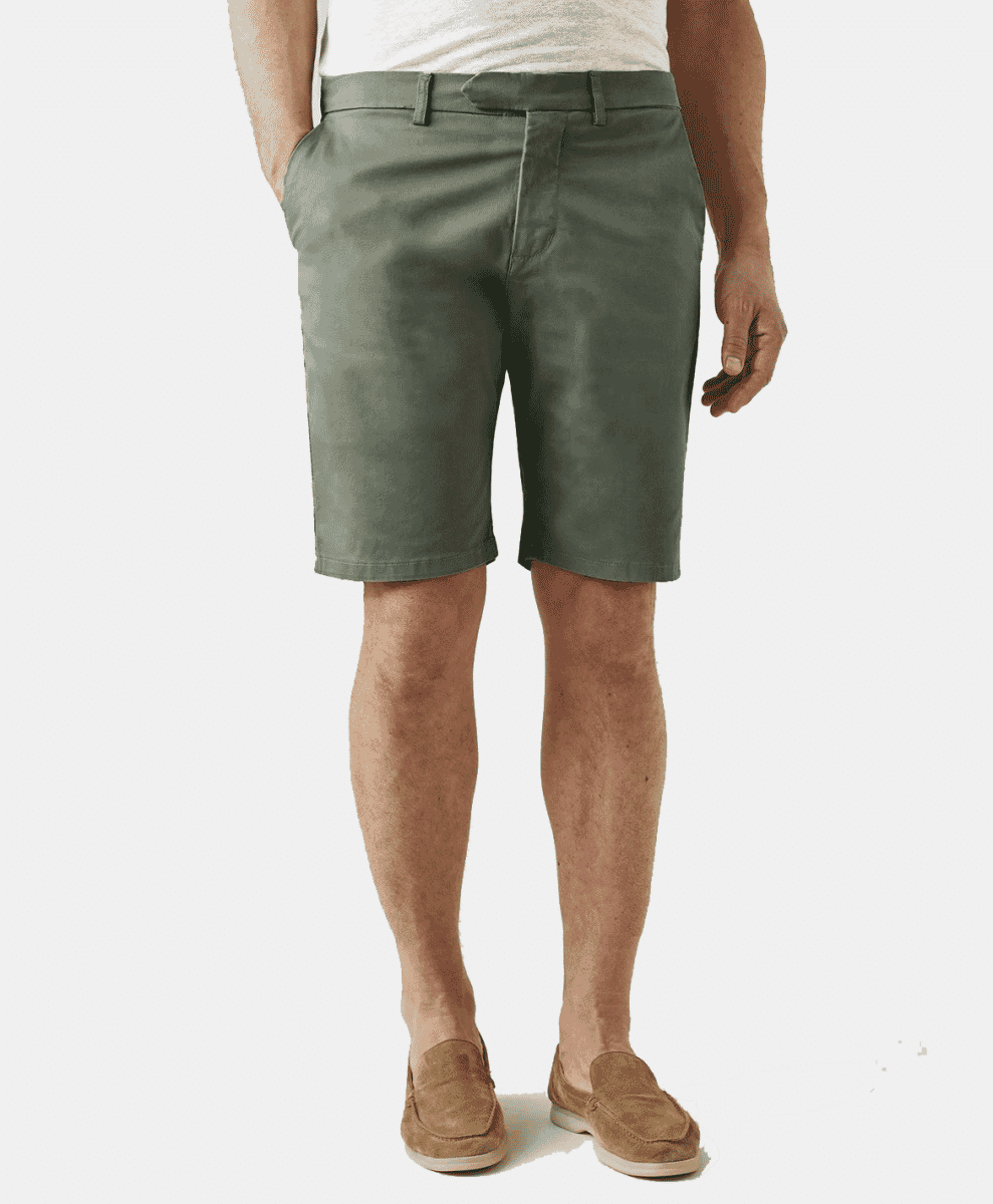 A man modeling olive green chino shorts with a white t-shirt and suede loafers.