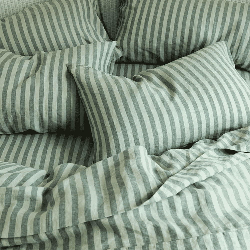 Close-up of green and white striped linen pillows and rumpled bedding.