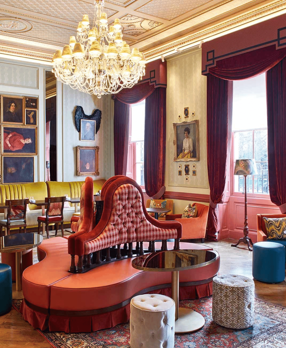 An opulent lounge with red tufted sofas, velvet curtains, and ornate chandeliers.