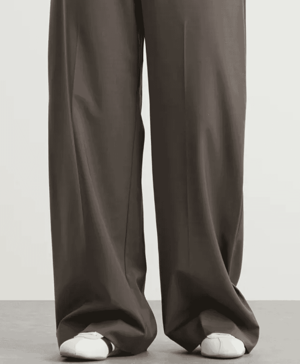 Person in wide-leg brown trousers wearing white ballet-style shoes.