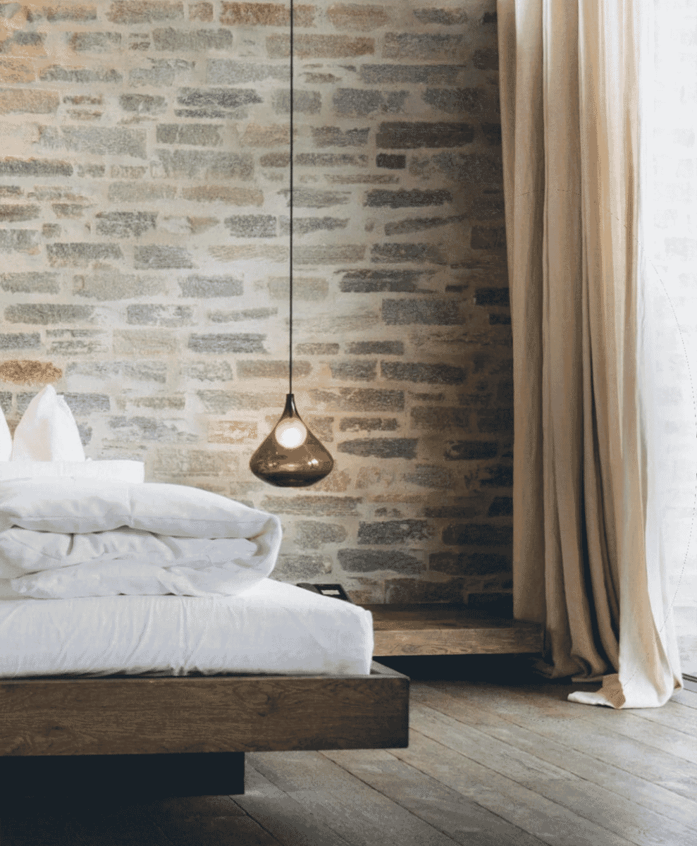 Minimalist modern bedroom featuring a natural stone wall and a hanging pendant lamp.
