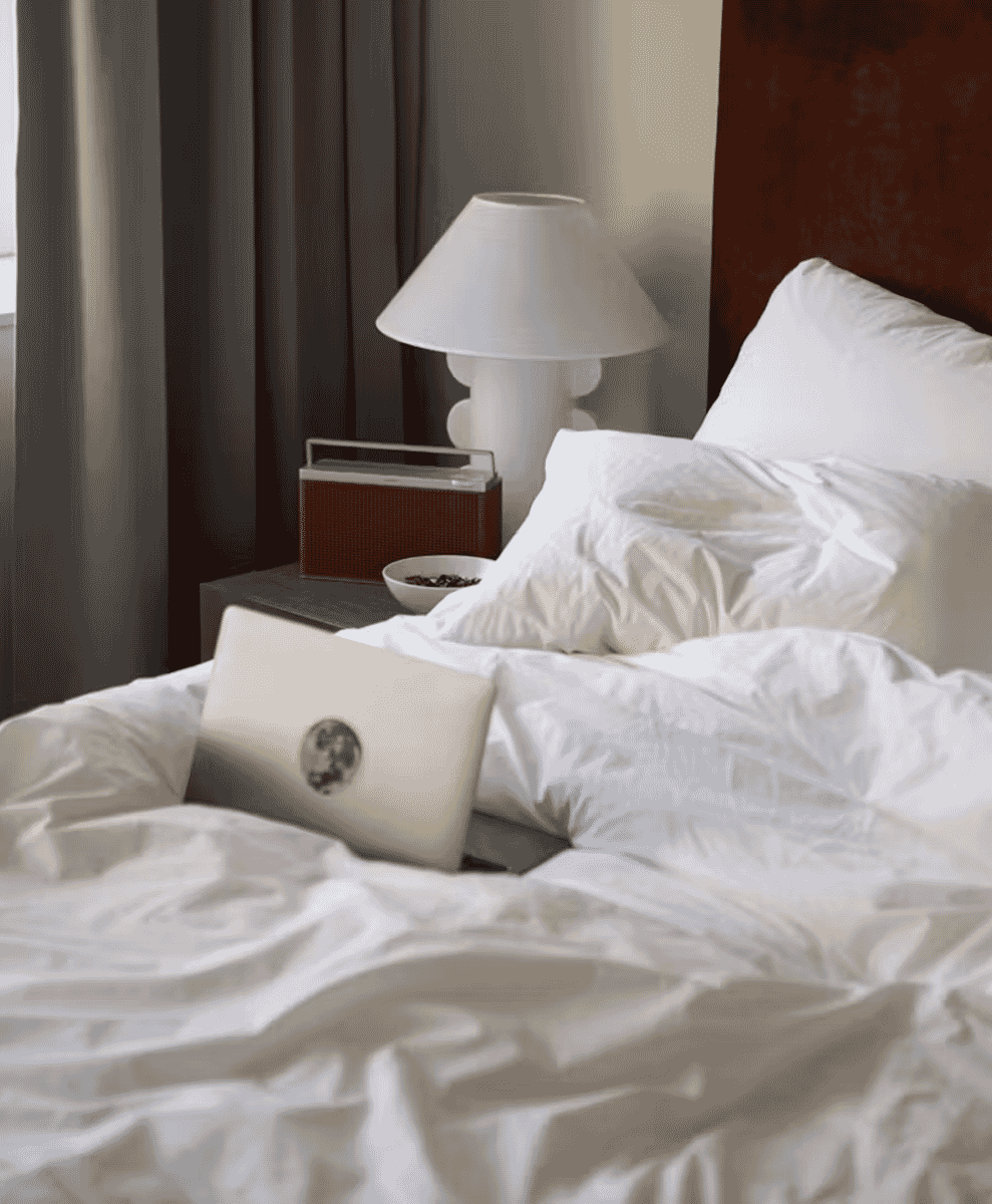A minimalist bedroom with white rumpled bedding and a laptop.