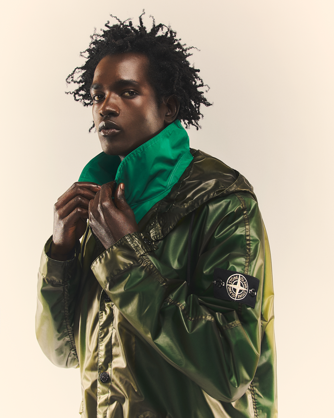 A model wearing the glossy olive-green bomber version of the jacket looking away in a studio setting.