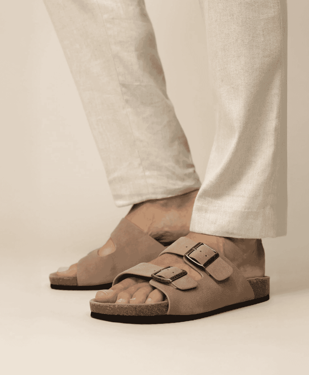 Person wearing beige suede double-strap sandals with light linen trousers