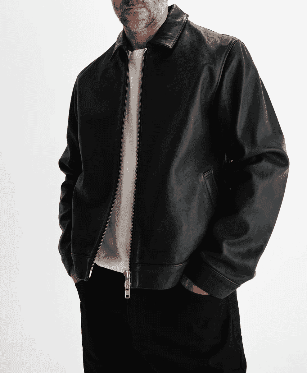 A man modeling a black leather bomber jacket over a light shirt against a white background.