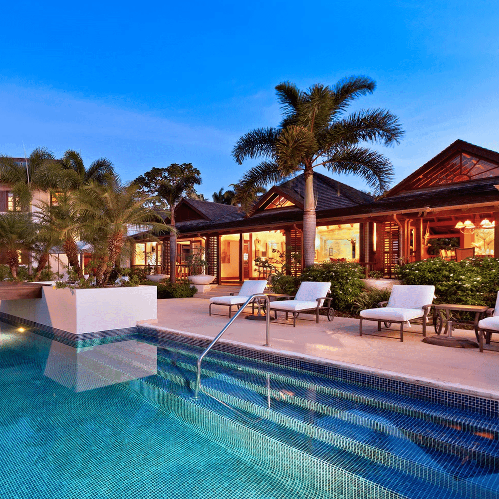 A tranquil twilight scene of an illuminated resort pool and villas surrounded by palm trees.