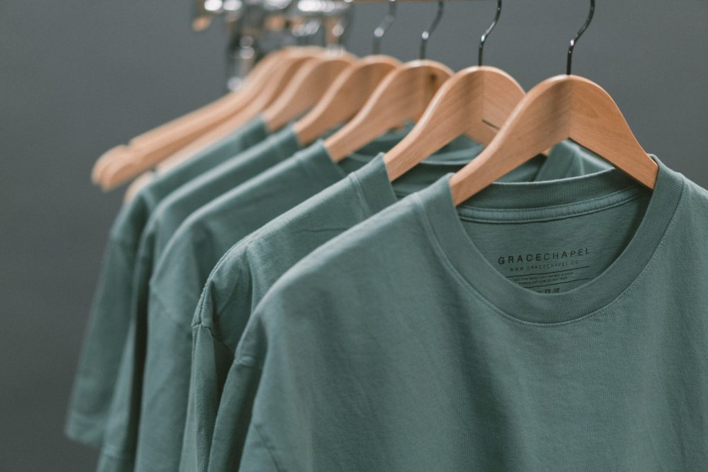 A row of olive green crew-neck T-shirts on wooden hangers with clear brand labels.