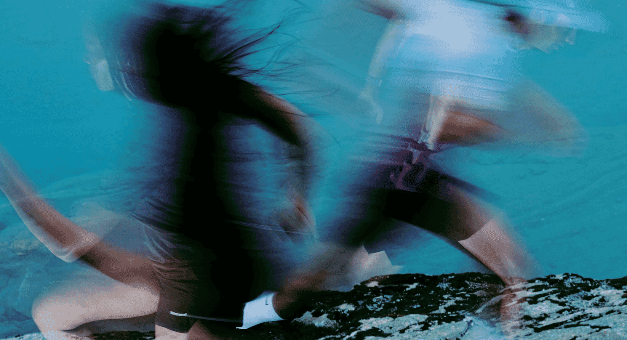Person in dark technical swimwear partially submerged in turquoise water with a motion-blur effect.