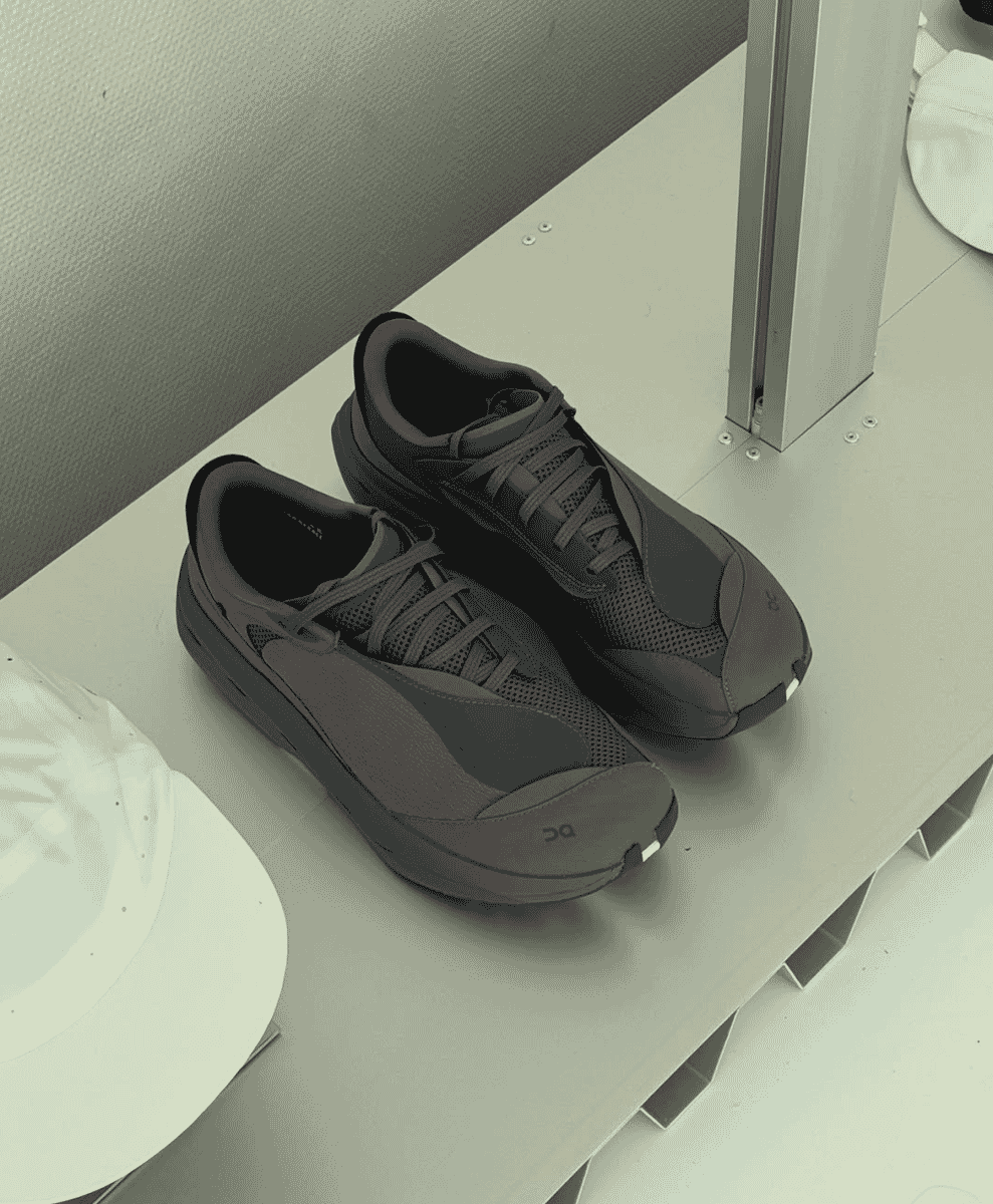 Dark gray ON running shoes and white caps displayed on a minimalist white shelf.