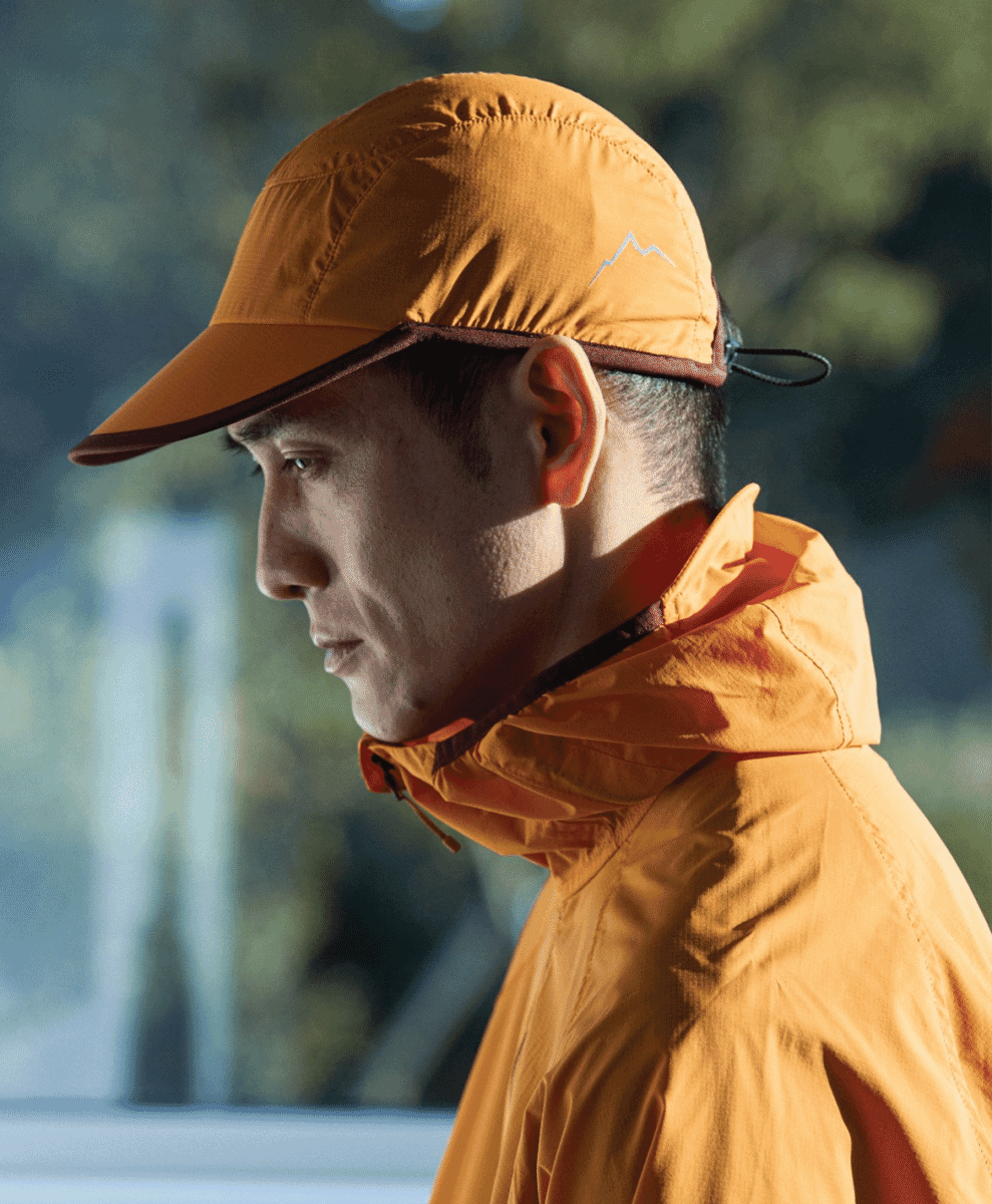 Profile view of a man wearing an orange technical outdoor cap with mountain branding