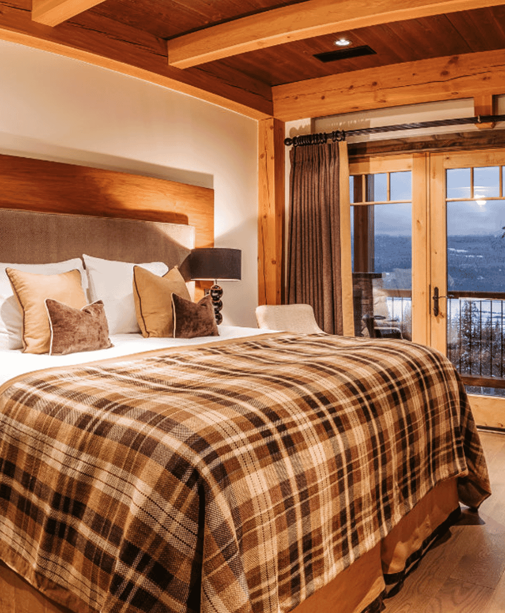 Cozy bedroom with plaid bedding and a large window looking out onto snowy mountains.