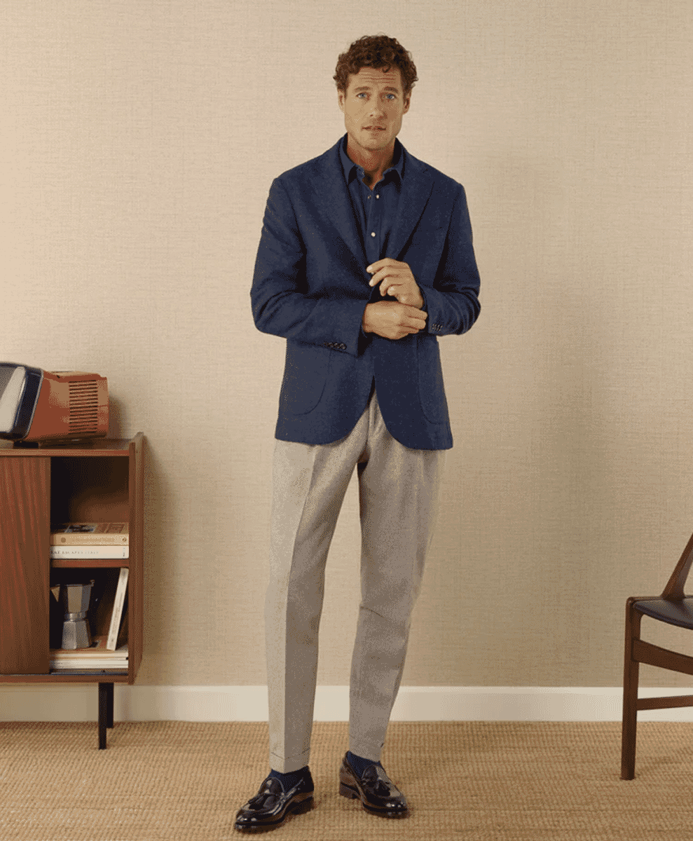 A man wearing a navy textured blazer with light gray trousers and loafers.