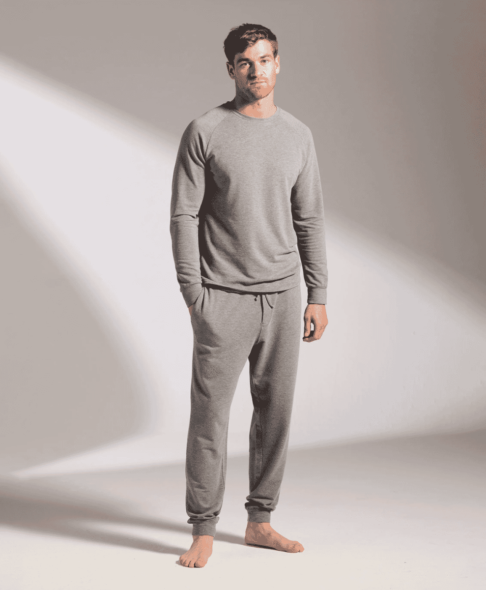 Man modeling a matching grey sweatshirt and sweatpants loungewear set.