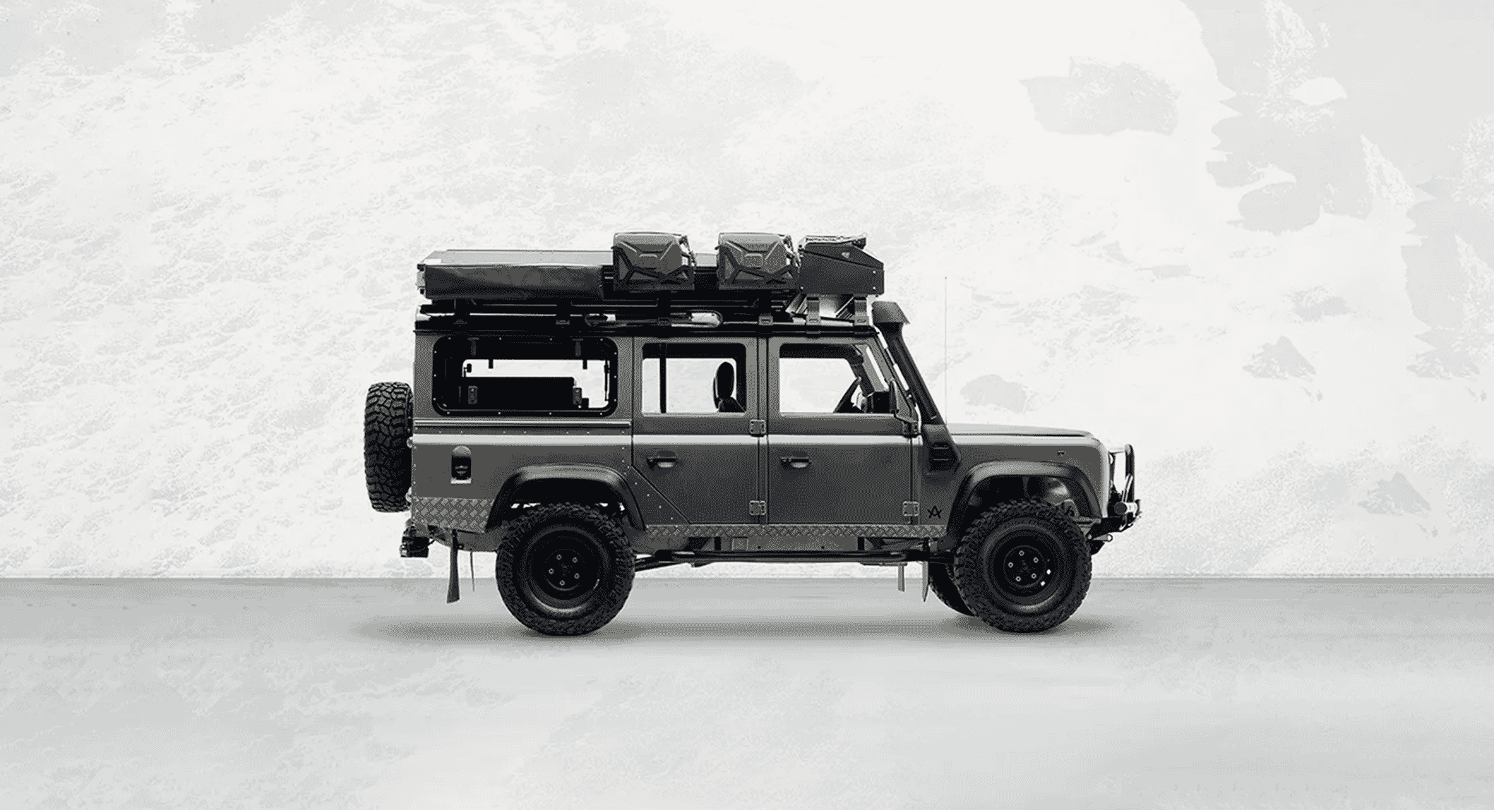 Black and white profile of a modified Land Rover Defender with a roof rack and rugged tires.