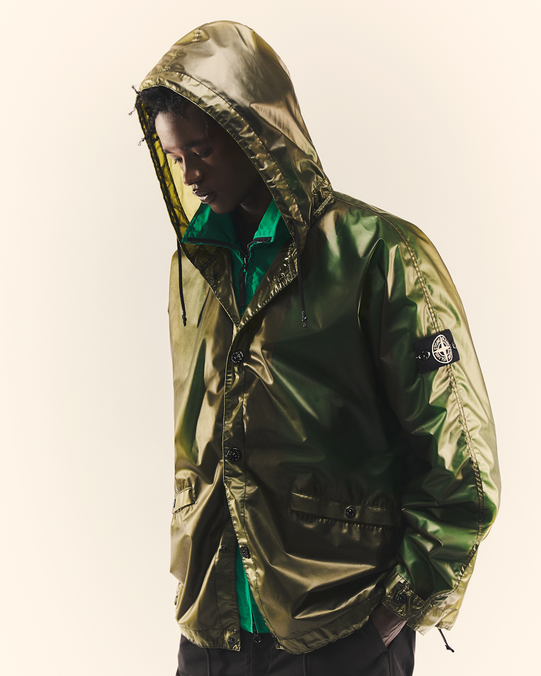 Full-body studio shot of a model wearing the glossy olive-green Stone Island hooded jacket.