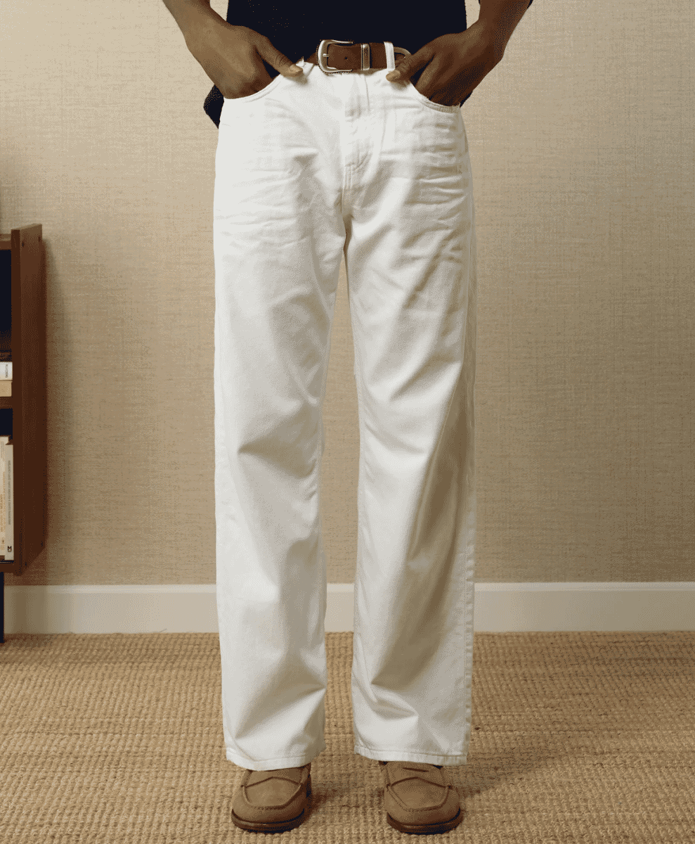 Man modeling white wide-leg jeans with a brown leather belt and tan loafers.