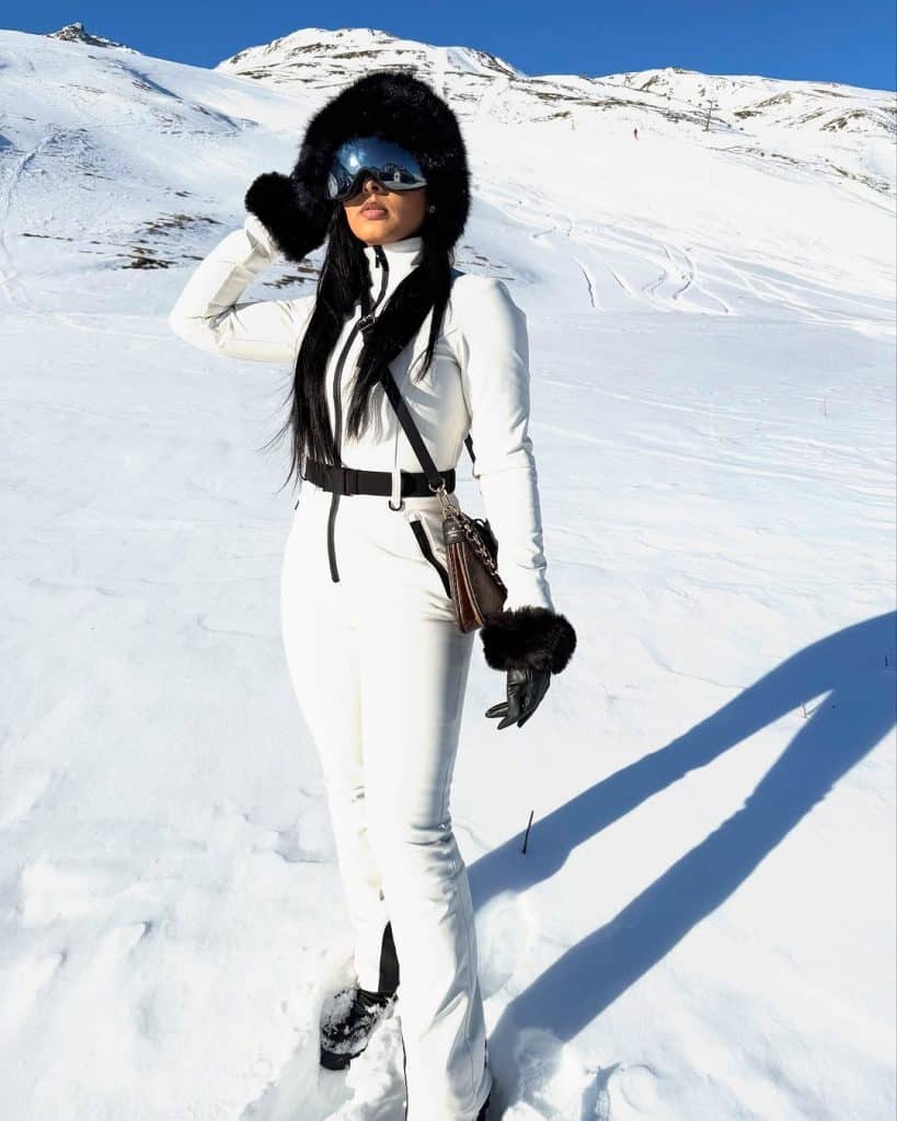 Woman in a white ski suit with a black fur-trimmed hat and reflective goggles.