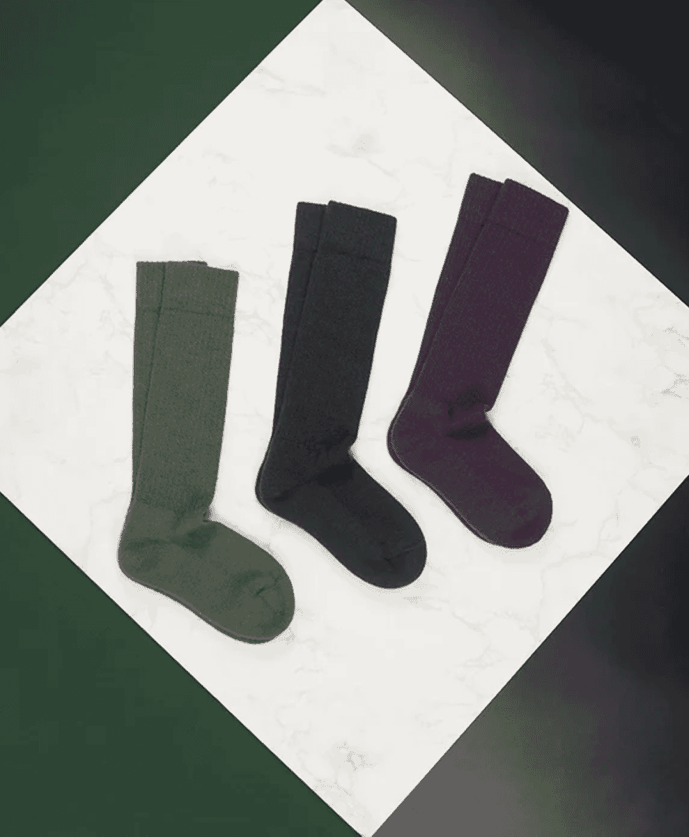 A display of olive, black, and purple knee-high wool socks on marble.