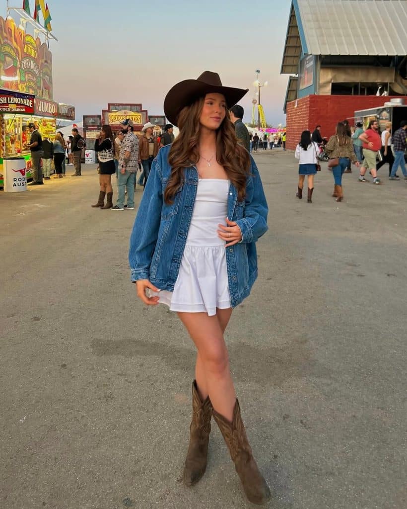 Woman in a cowboy hat and denim jacket posing at a fairground.