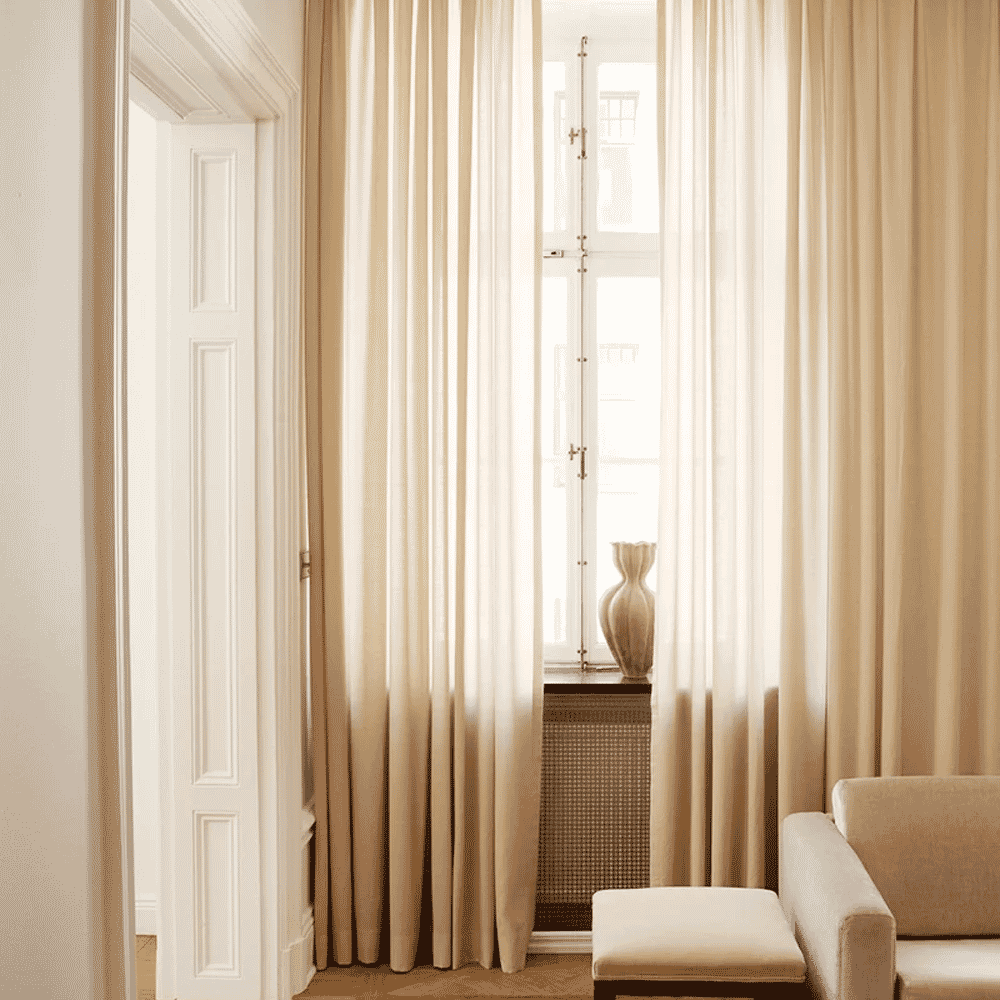 Softly lit room with cream-colored drapes framing a large window.