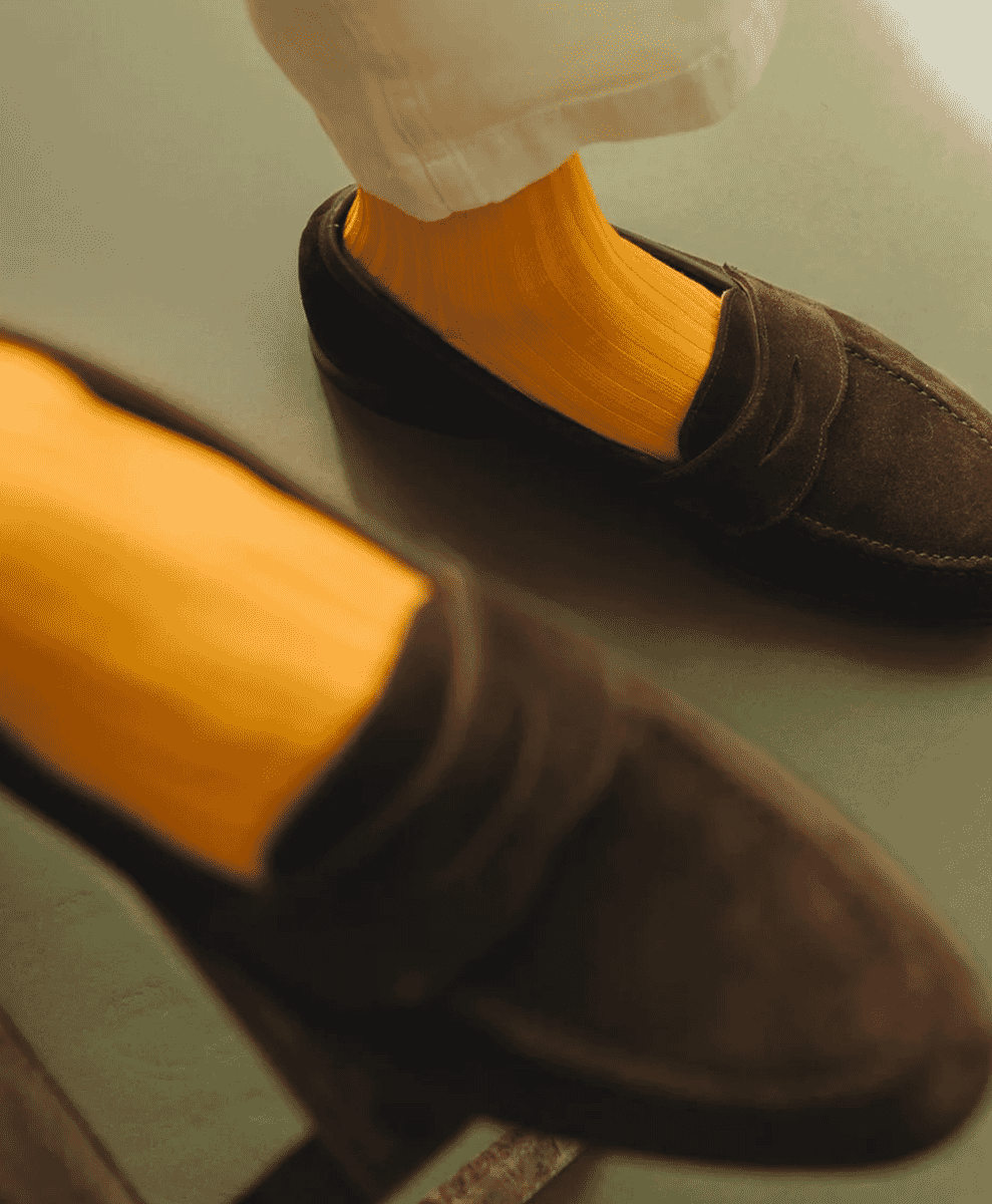 Close-up of mustard-yellow ribbed socks worn with brown suede loafers.