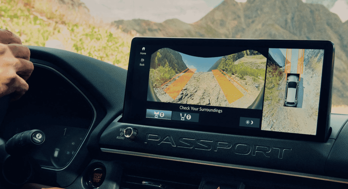 Interior view of a car dashboard with vehicle tech and mountain landscape visible through the windshield.