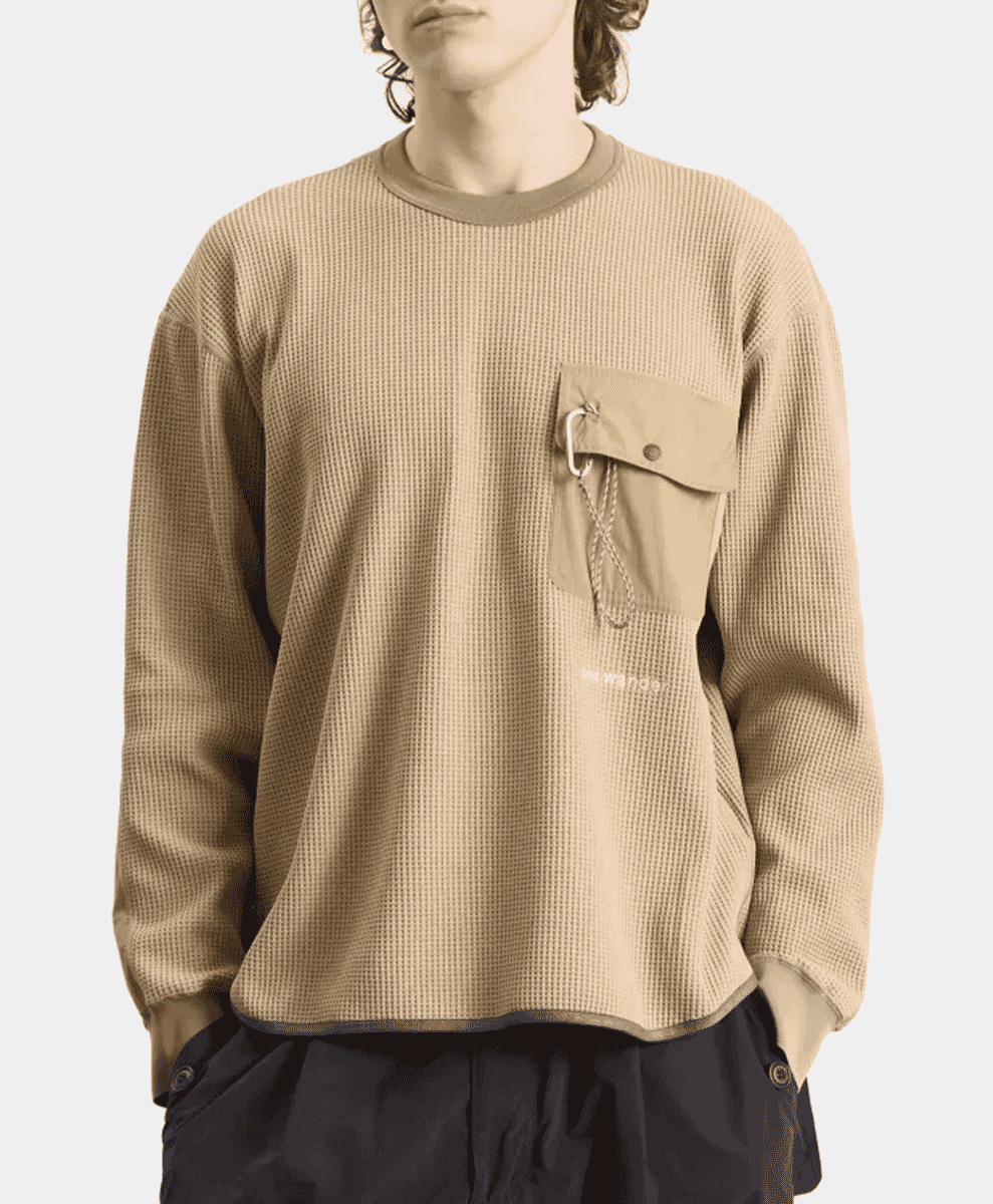 A model wearing a beige waffle knit long-sleeve shirt paired with dark trousers.