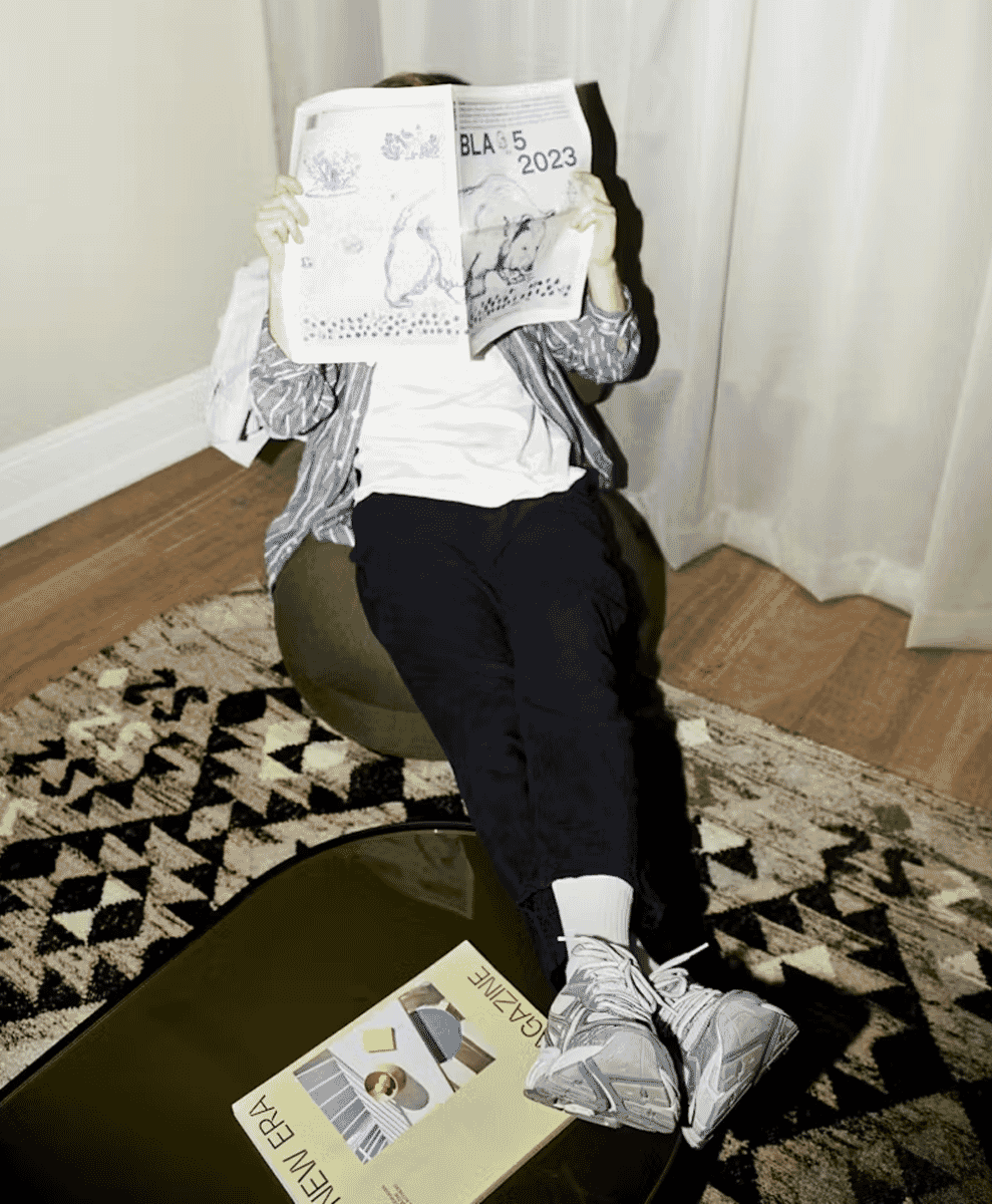 A person in a striped shirt lounging on a bean bag chair reading a magazine.