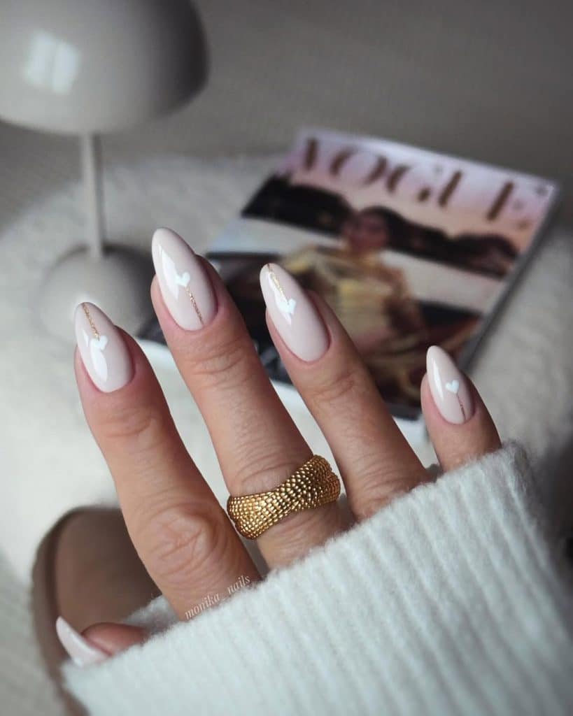 Nude-pink nails with tiny gold heart accents and a gold ring.
