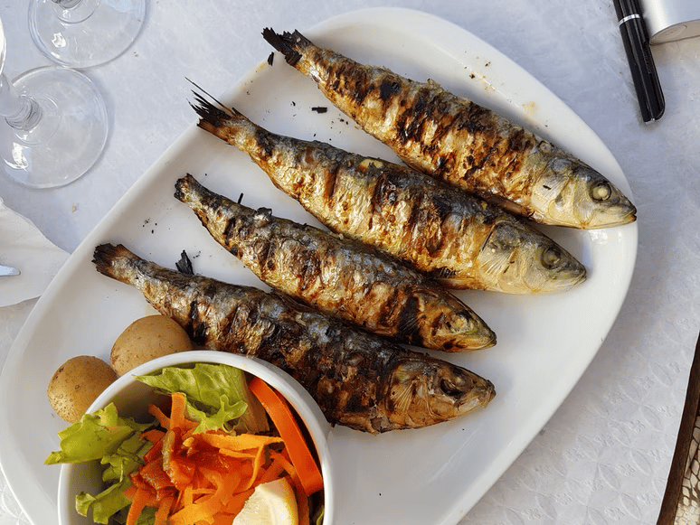 A plate of grilled fish with salad and potatoes served at an outdoor table.