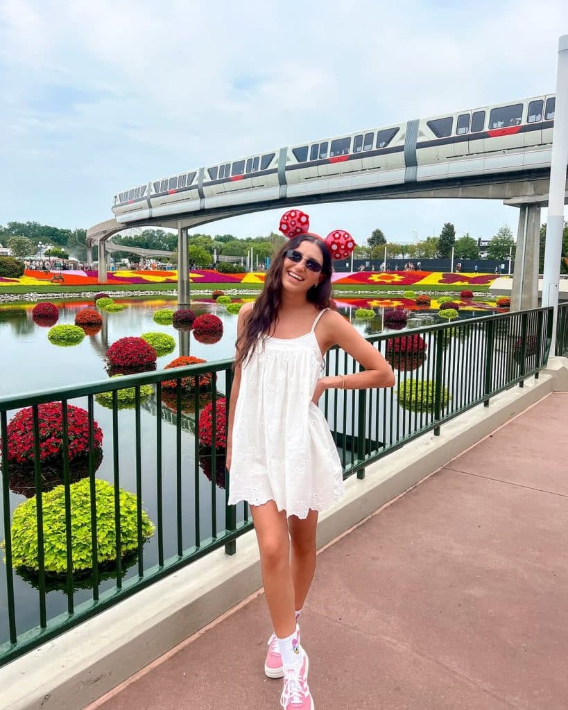 A woman in a white eyelet sundress and pink sneakers by a flower-lined canal.