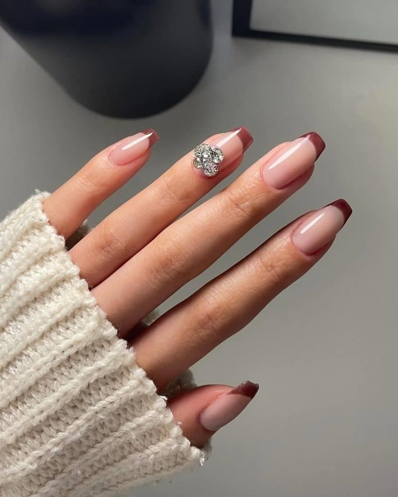 Nude and burgundy French manicure with a rhinestone accent on the ring finger.