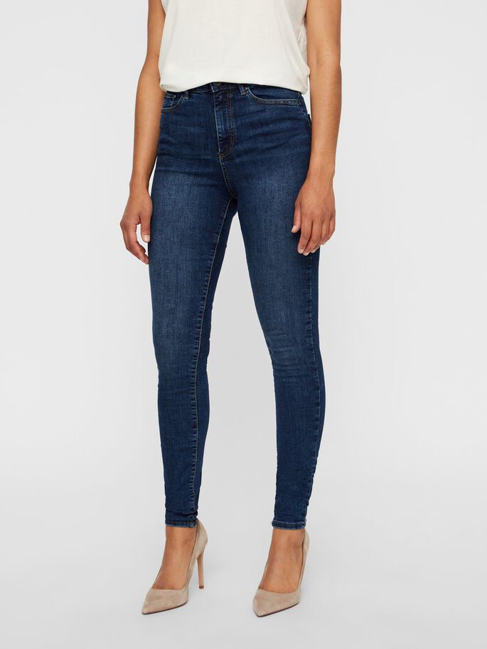 Woman modeling dark blue high-waisted skinny jeans with beige heels.
