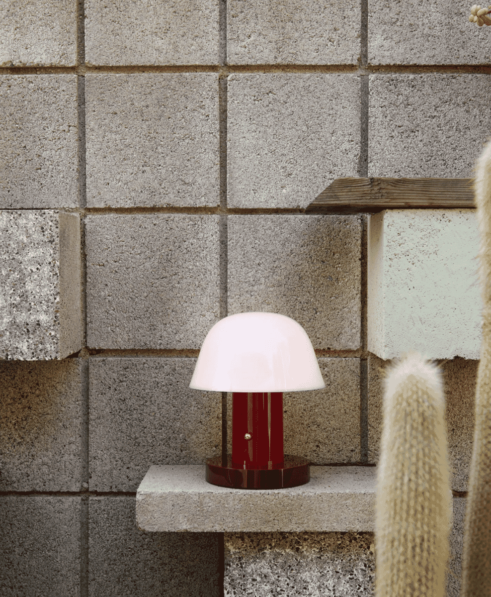 Mushroom-shaped table lamp with a white dome and maroon base on a concrete shelf.