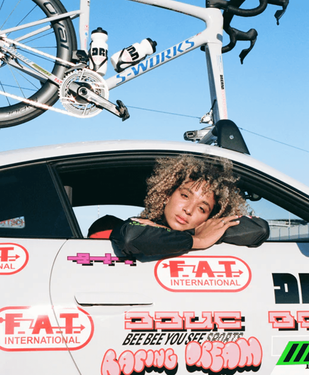 A woman in a black athletic jacket leaning out of a white racing car window with a white S-Works bike mounted on the roof.