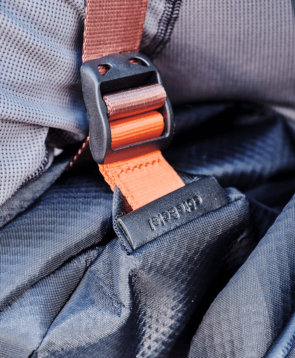 Macro shot of an orange webbing strap and black plastic buckle on a grey textured bag.