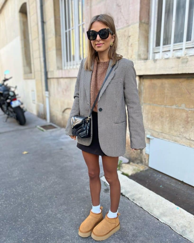 Woman wearing a houndstooth blazer and black mini skirt paired with chunky tan boots in an urban setting.