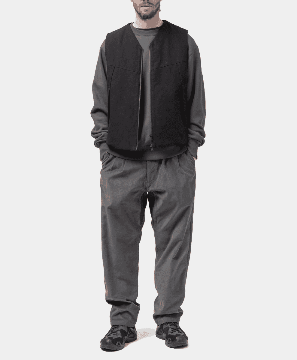 A man in a black vest, grey sweatshirt, and graphite corduroy pants.