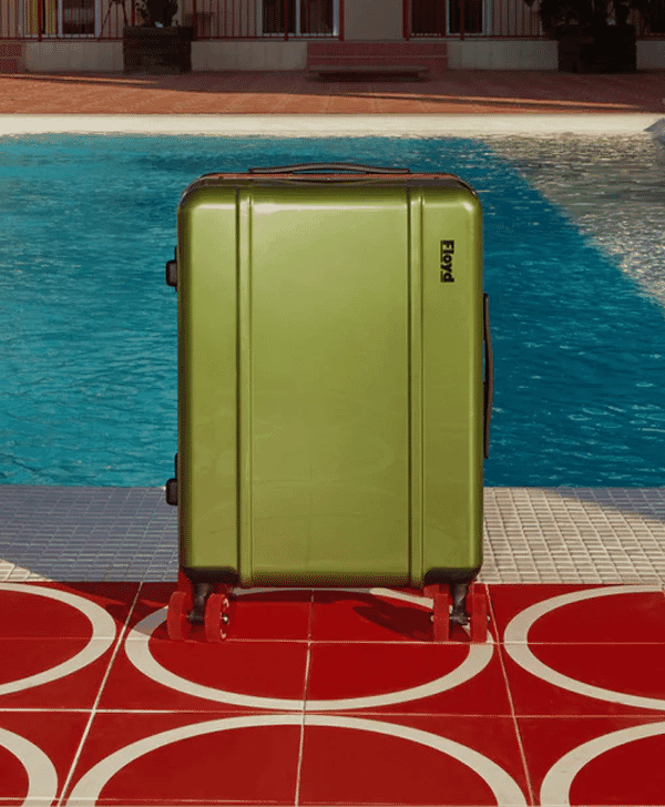A green hard-shell rolling suitcase by a blue swimming pool.
