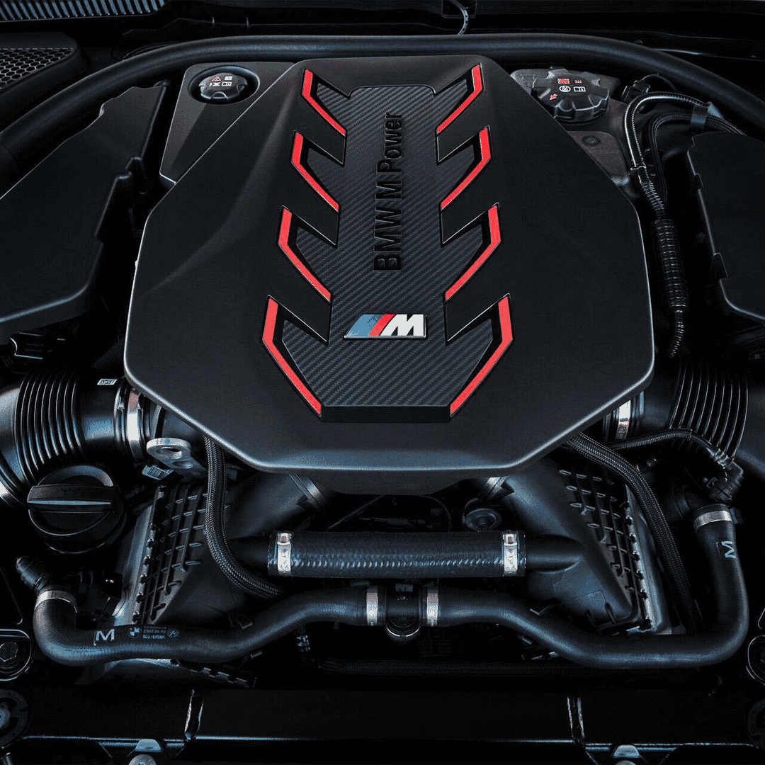 A close-up of the BMW M Power engine cover featuring carbon fiber texture and red accents.