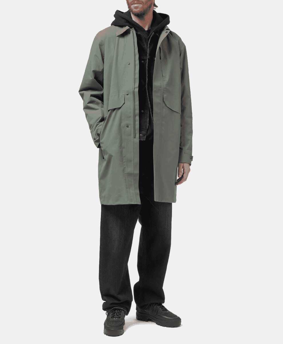 Man modeling a longline sage green technical coat with a hood.