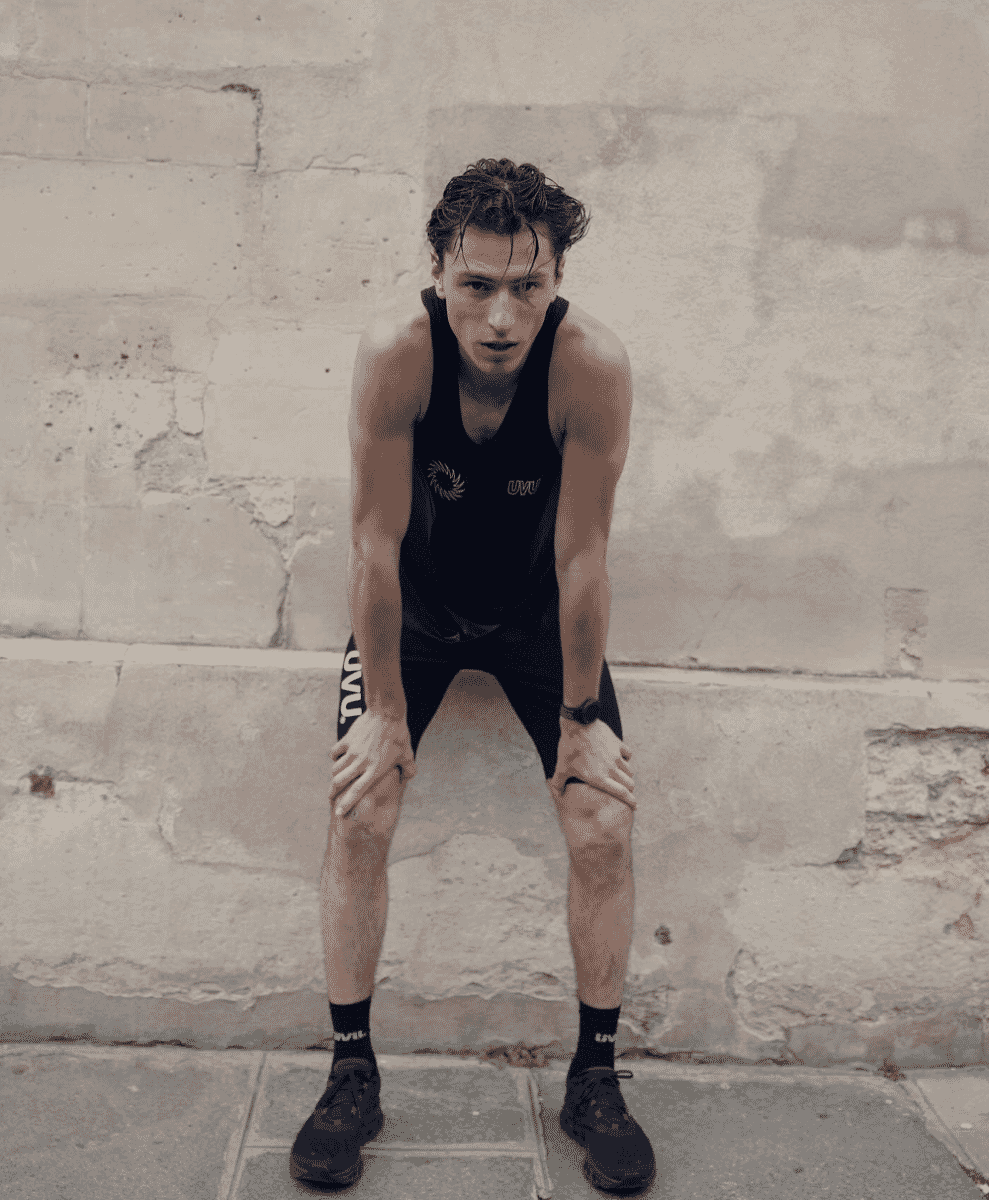 A runner in a UVU technical tank top posing against a weathered stone wall.