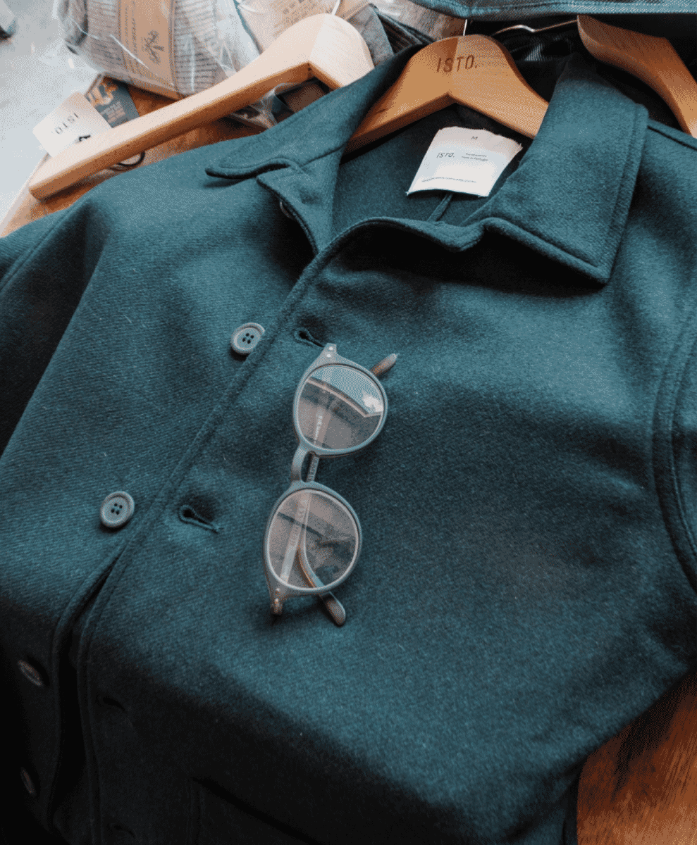 Close-up of a teal wool jacket on a wooden hanger with the ISTO. brand label visible