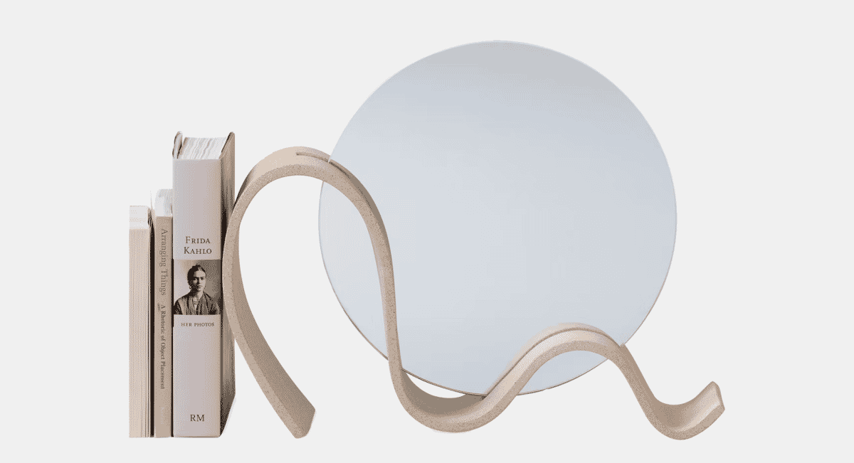 Round mirror with a sculptural beige base sitting next to a stack of books.